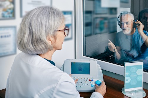 Audiologist giving hearing test to man in booth