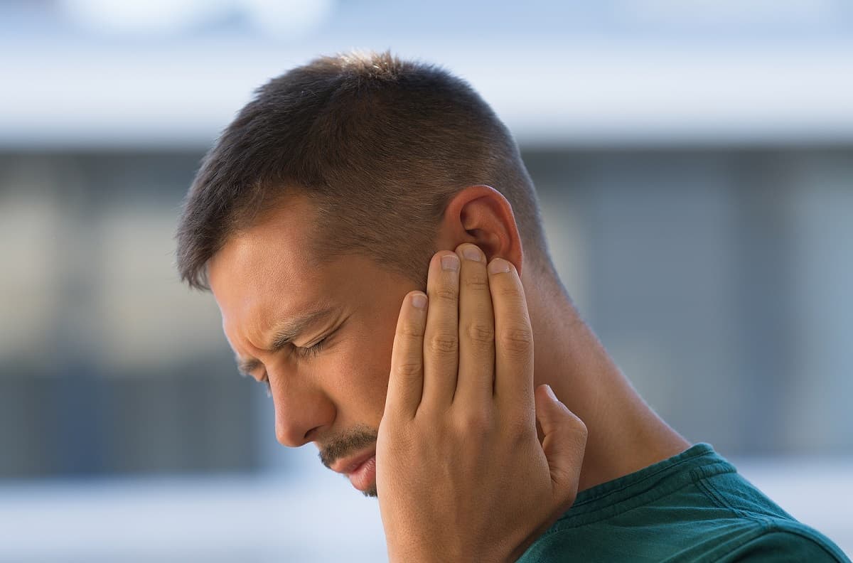 man holds ear as he tries to deal with pain.